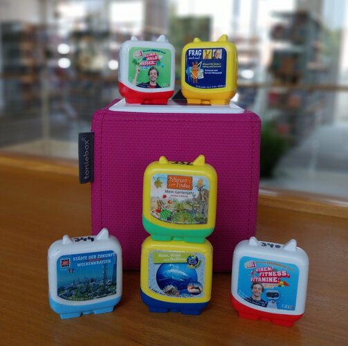 Tonieboxen und Figuren auf pinkfarbenem Podest in der Kinderbibliothek.