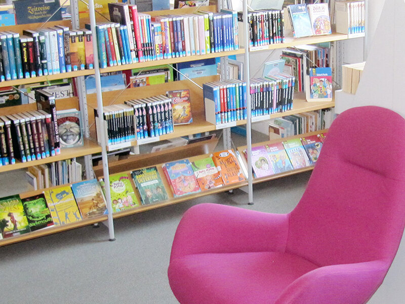 Lesesessel in freundlicher Ecke mit Bücherwand und bunten Kinderbüchern.