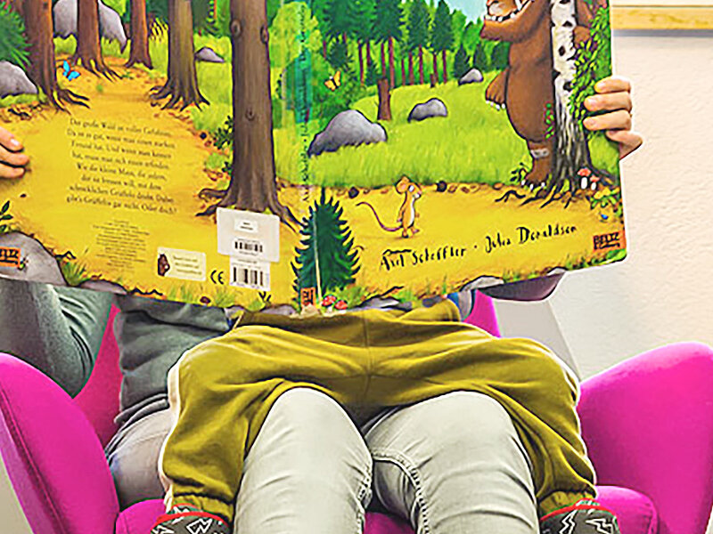 Zwei Kinder sitzen in der Kinderbibliothek und lesen in buntem Umfeld.