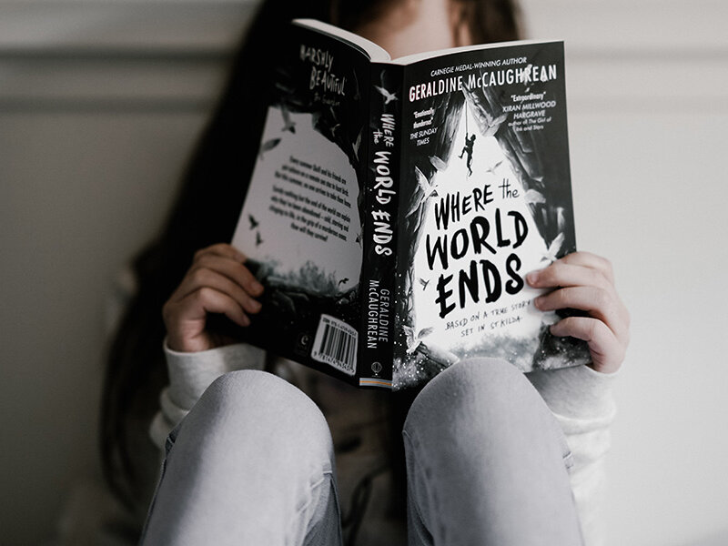 Teenager mit Hoodie, Buch und Stofftasche vor heller Wand.
