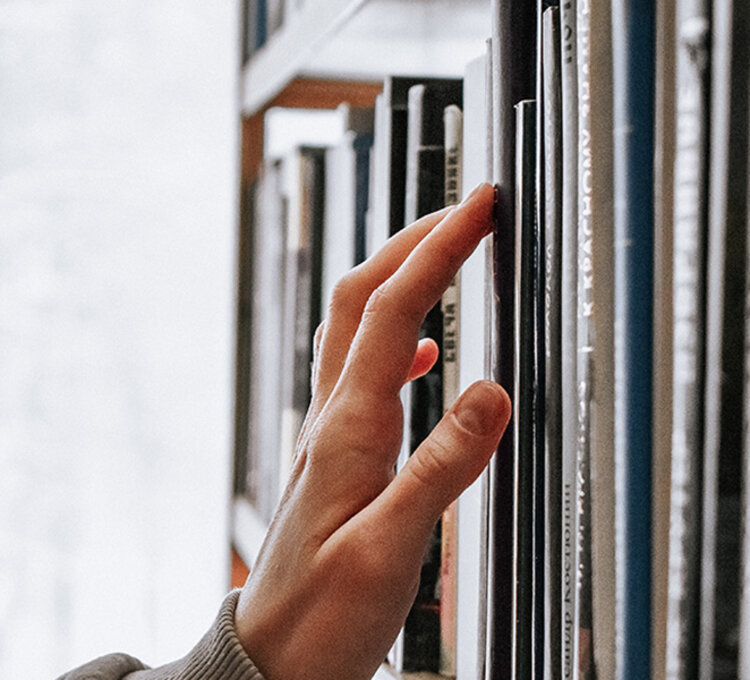 Hand zieht ein Buch aus einem vertikalen Regal in der Bibliothek.