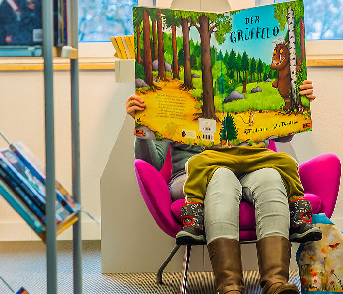 Gemütliche Leseecke mit zwei Kindern auf Sitzsäcken vor buntem Bücherregal.