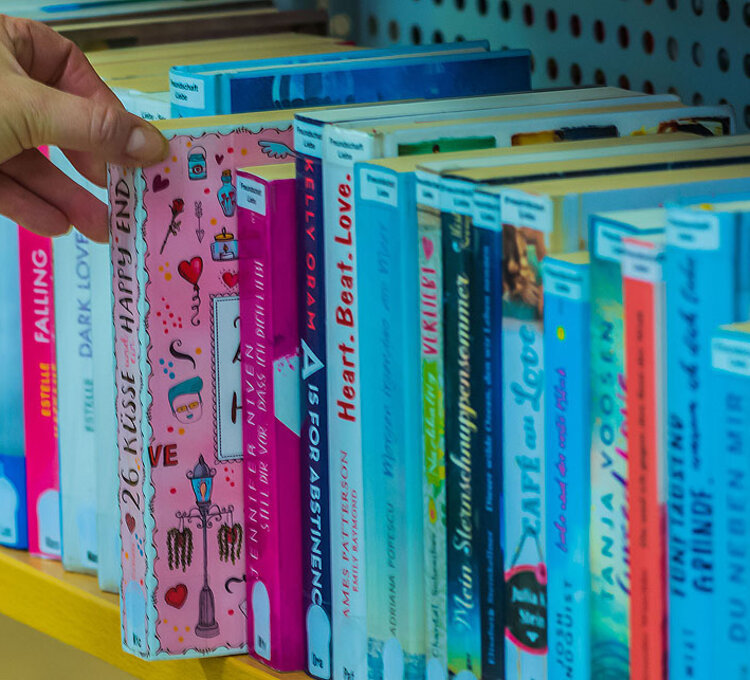 Hand greift nach buntem Kinderbuch in Bücherregal.
