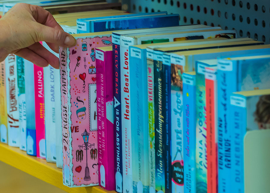 Kinderbuch im Regal Hand greift nach buntem Kinderbuch in Bücherregal.