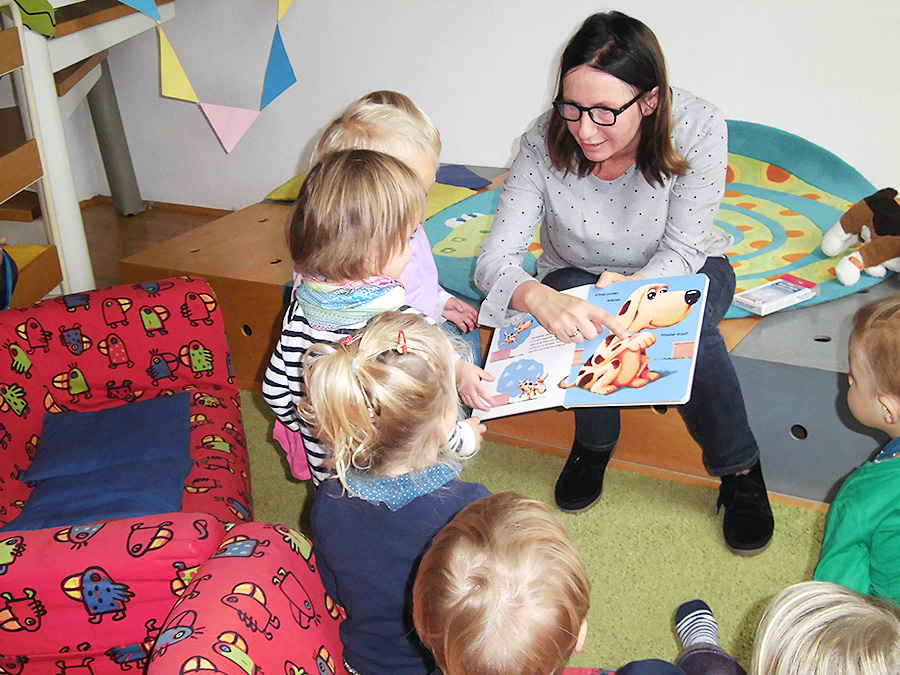 Erzieherin liest mehreren Kindern im Sitzkreis ein Buch vor.